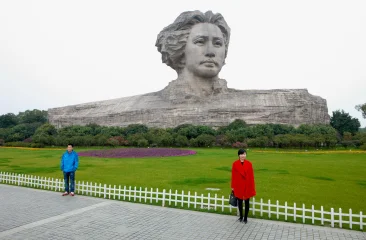 A woman in a red coat and a man in a blue jacket stand in front of a large statue.